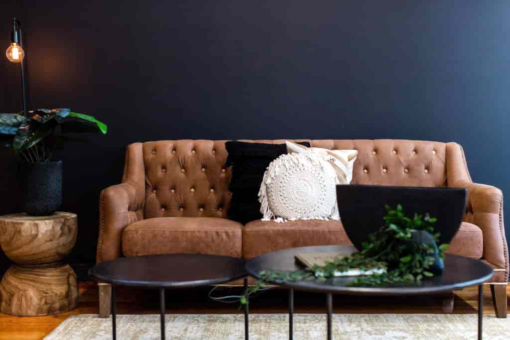 Two round coffee tables in front of brown leather lounge with brown and white pillows
